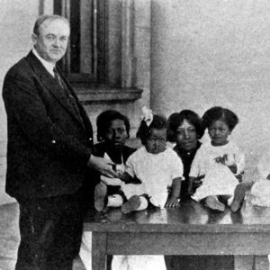 White man standing in suit with African-American women and children sitting beside him