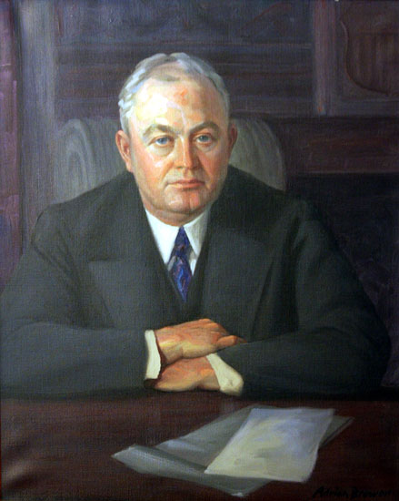 White man in suit sitting at his desk with his arms crossed