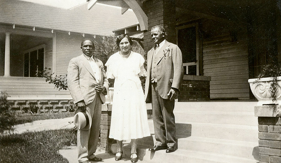 Two African-American men in suits with woman in dress outside house