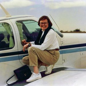 White woman with hand bag on the wing of a a propeller-driven airplane
