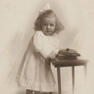 Young white girl in dress with bow in her hair playing with toy on small table