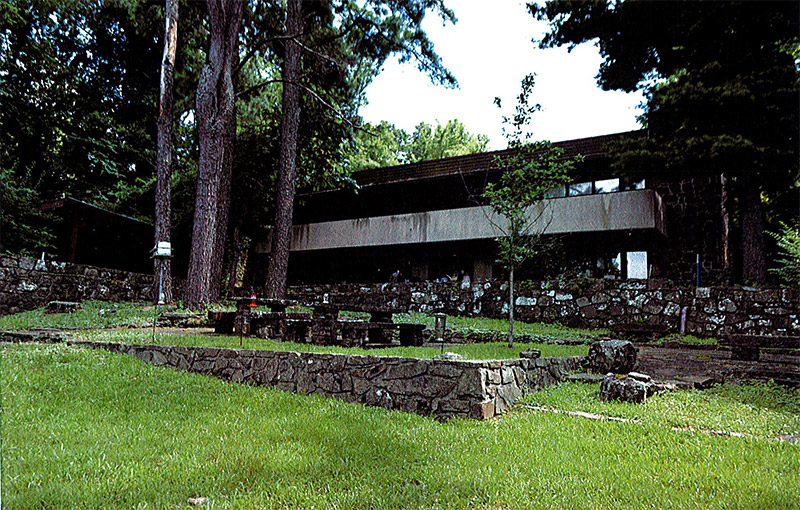 Multistory house with covered porch and flat roof with stone walls and benches in the foreground