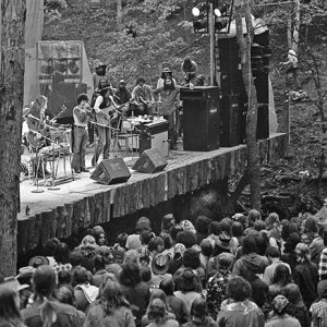Musicians performing on large wooden stage to large crowd