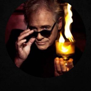 White man with sunglasses holding a glass cup with fire in it