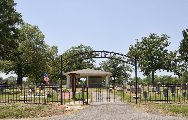 Cemetery with iron gate and building and flag on gravel road