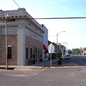 Street with buildings on both sides and trees and railroad crossing in the background