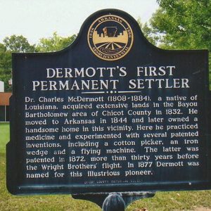 "Dermott's First Permanent Settlement" historical marker sign with trees and building behind