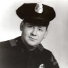 dark-eyed white man in police uniform with cap and badge