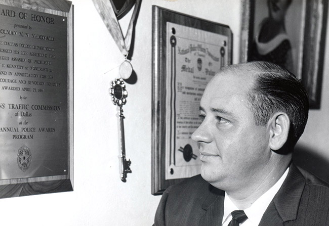 White man in suit and tie looking at award plaques on wall