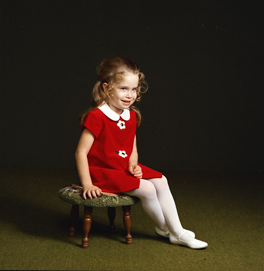 Young white girl in red dress sitting on a stool smiling