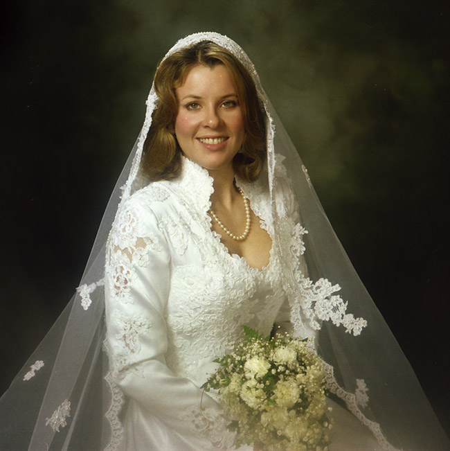 white woman smiling in wedding dress with veil and flowers