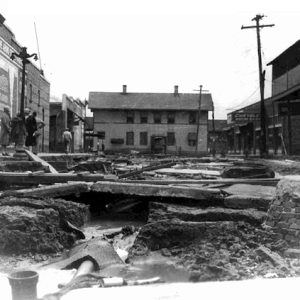 Damaged street surrounded by two-story town buildings with people on sidewalk