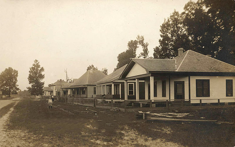 Child standing on street in front of single-story houses with covered porches
