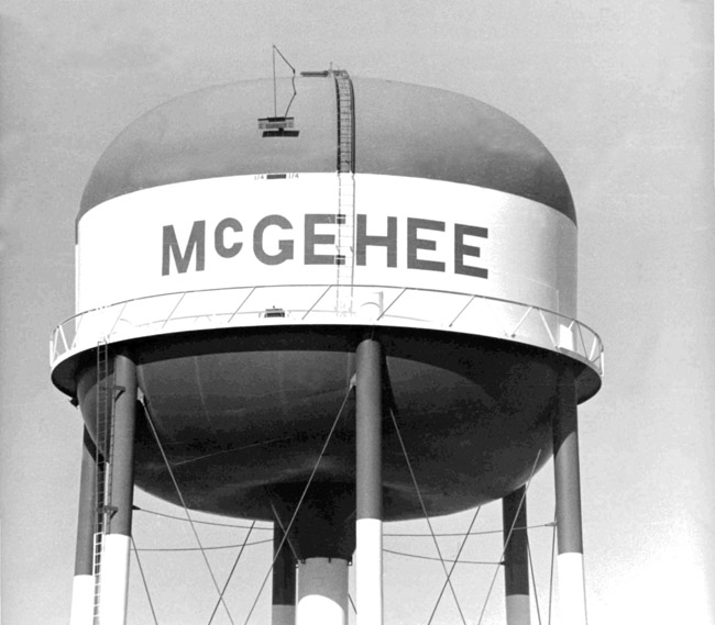 top of massive water tower with seven legs ladders and surrounding walkway painted "McGehee" in large letters.