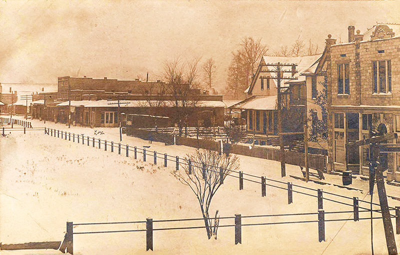 Multistory town buildings on snow covered streets with fenced-in park in the foreground