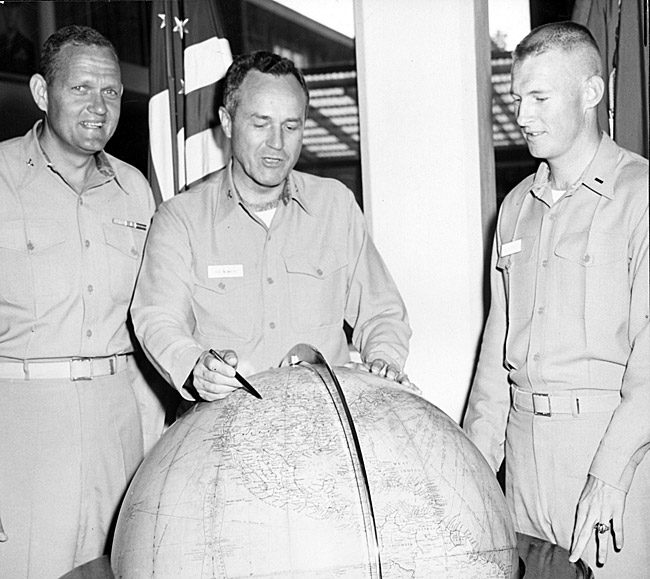 Three white men in military uniform examingin globe with American flag in the background