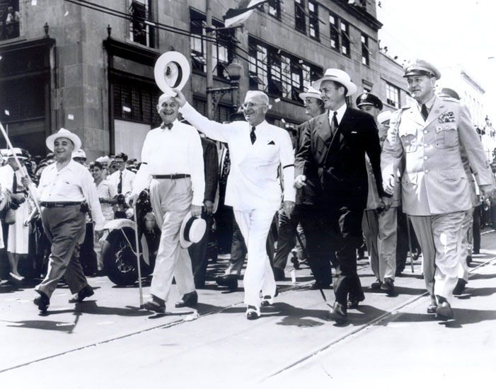 White men in suits and hats leading a parade down city street