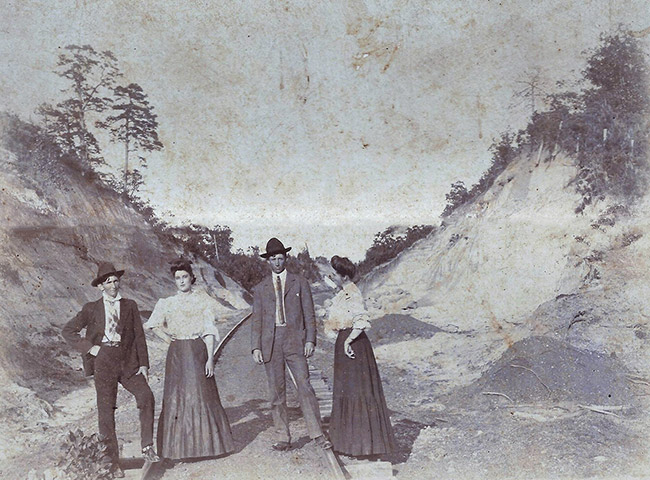 Two white men in suits and hats posing with two white women in dresses in railroad cut standing between two hills