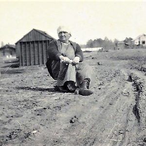 White woman sitting on dirt road with buildings in the background