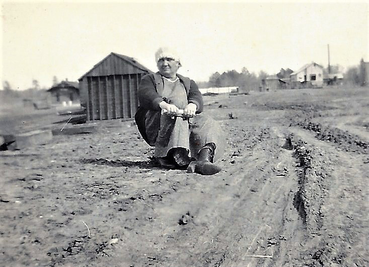 White woman sitting on dirt road with buildings in the background