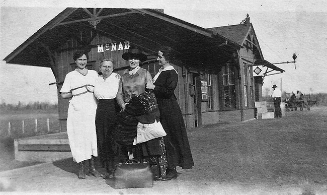 Four white women posing together at train depot building