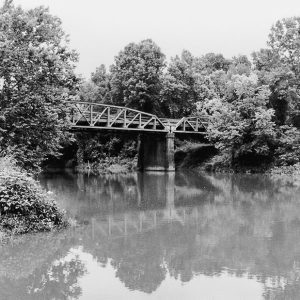Steel arch truss bridge over large creek with trees around it