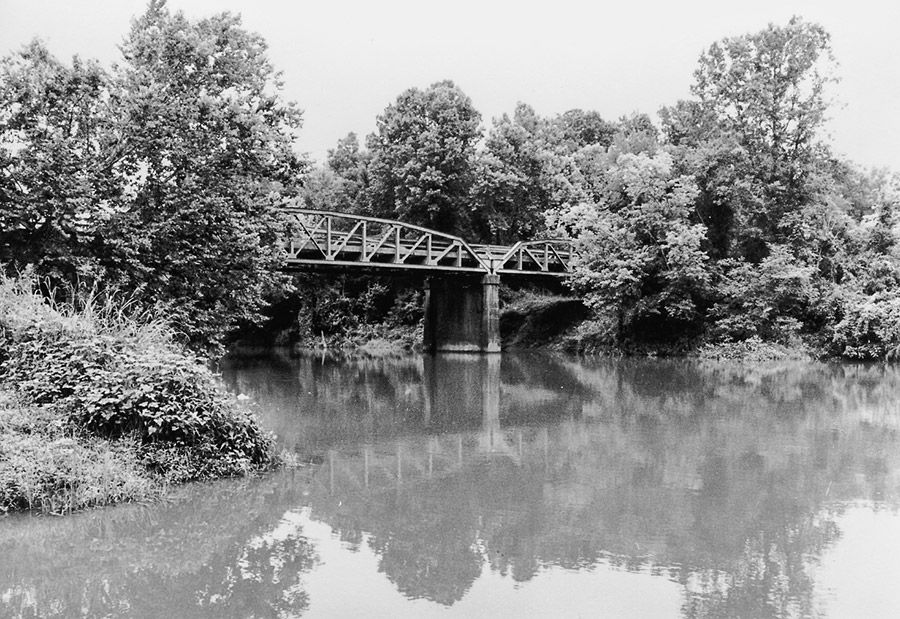 Steel arch truss bridge over large creek with trees around it