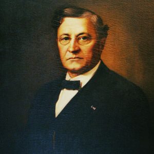 White man with glasses in black suit and bow tie