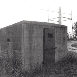 Small concrete building with iron door and water tower in the background