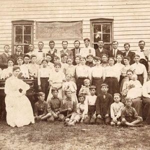 Young white students and faculty posing together outside building with wood siding and windows