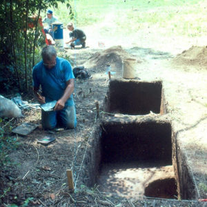 White men and woman documenting a dig site near mounds