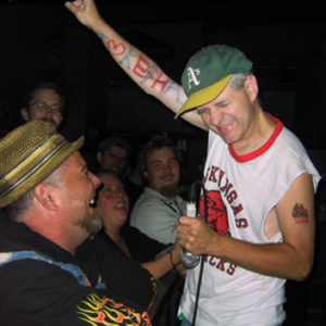 White man in hat with tattoos on stage with white crowd
