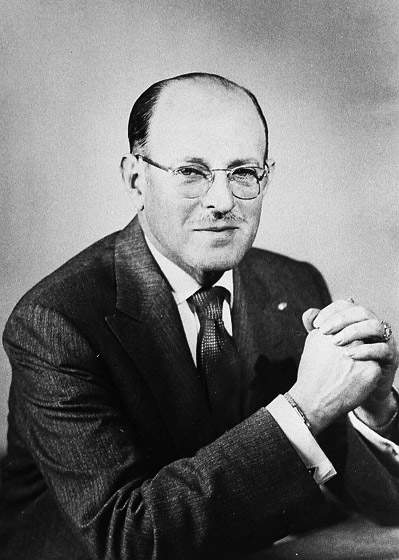 white man in glasses posed with hands folded in front