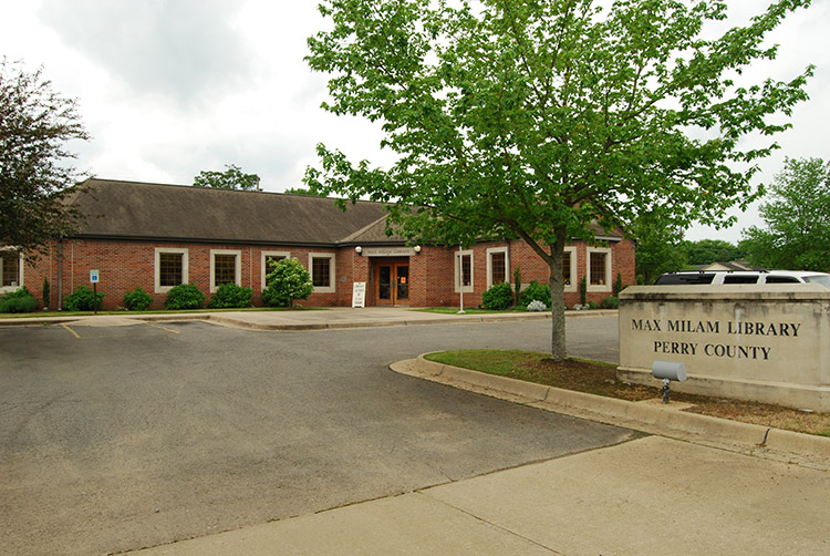 Single-story brick building on parking lot with tree and sign
