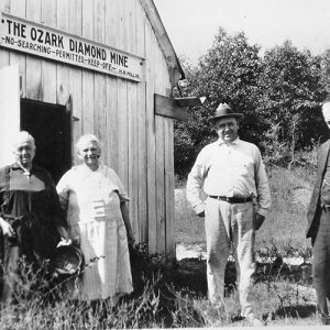 Two white men, one older than the other, and two older white women in front of a building with an open door and a sign saying "no searching permitted keep off"