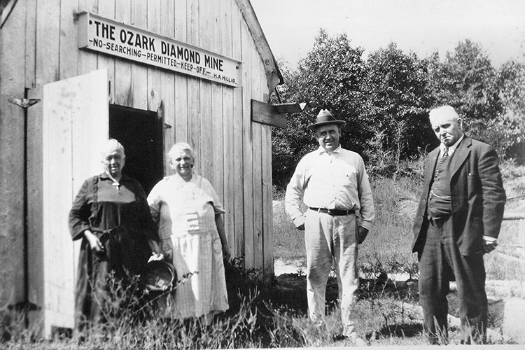 Two white men, one older than the other, and two older white women in front of a building with an open door and a sign saying "no searching permitted keep off"