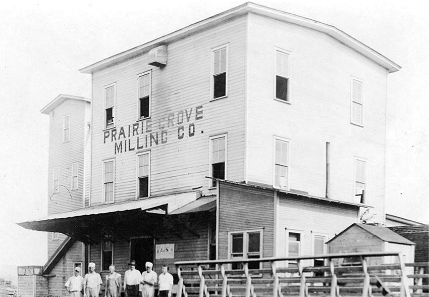 White men standing before large building "Prairie Grove Milling Company"