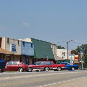 Storefronts and parked cars with gas station on street