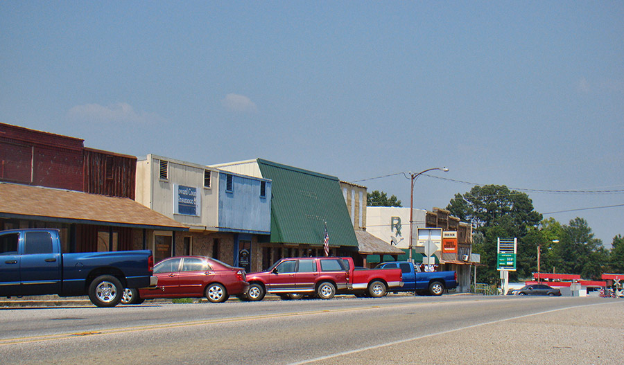 Storefronts and parked cars with gas station on street