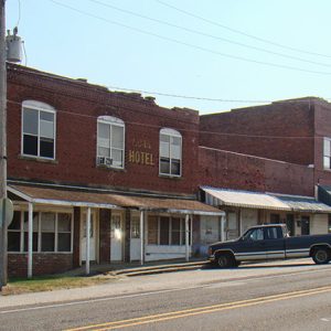 Two-story brick hotel and brick storefronts on street with cars
