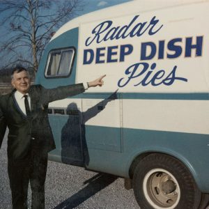 White man in suit and tie pointing at "Radar deep dish pies" advertisement on a recreational vehicle