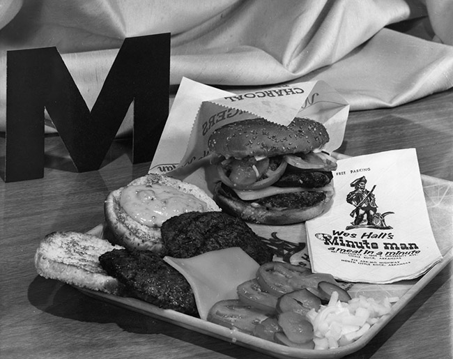 Hamburger and toppings displayed on a food tray with "Wes Hall's Minute Man" napkins and letter "M"