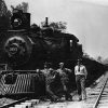Two rail workers and man in tie pose on tracks by locomotive 2633