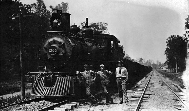 Two rail workers and man in tie pose on tracks by locomotive 2633