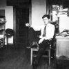 Young white man in shirt and tie sitting in an office with his leg p on the chair and smoking a cigarette