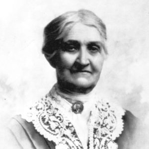 Older white woman wearing a dress with a portrait brooch and lace collar