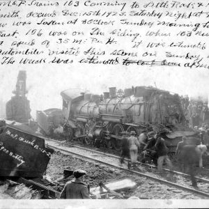 Crowd gathered around wrecked steam locomotive with writing above the image
