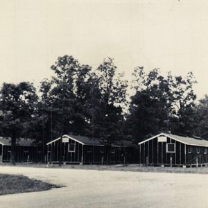 Barrack buildings amid trees and road with fence