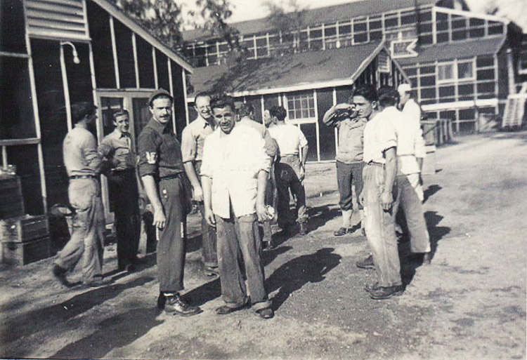 Young white men standing outside barracks buildings