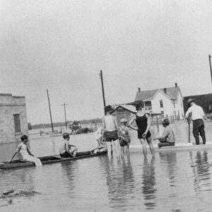 White men women and children in boats and standing in flooded street